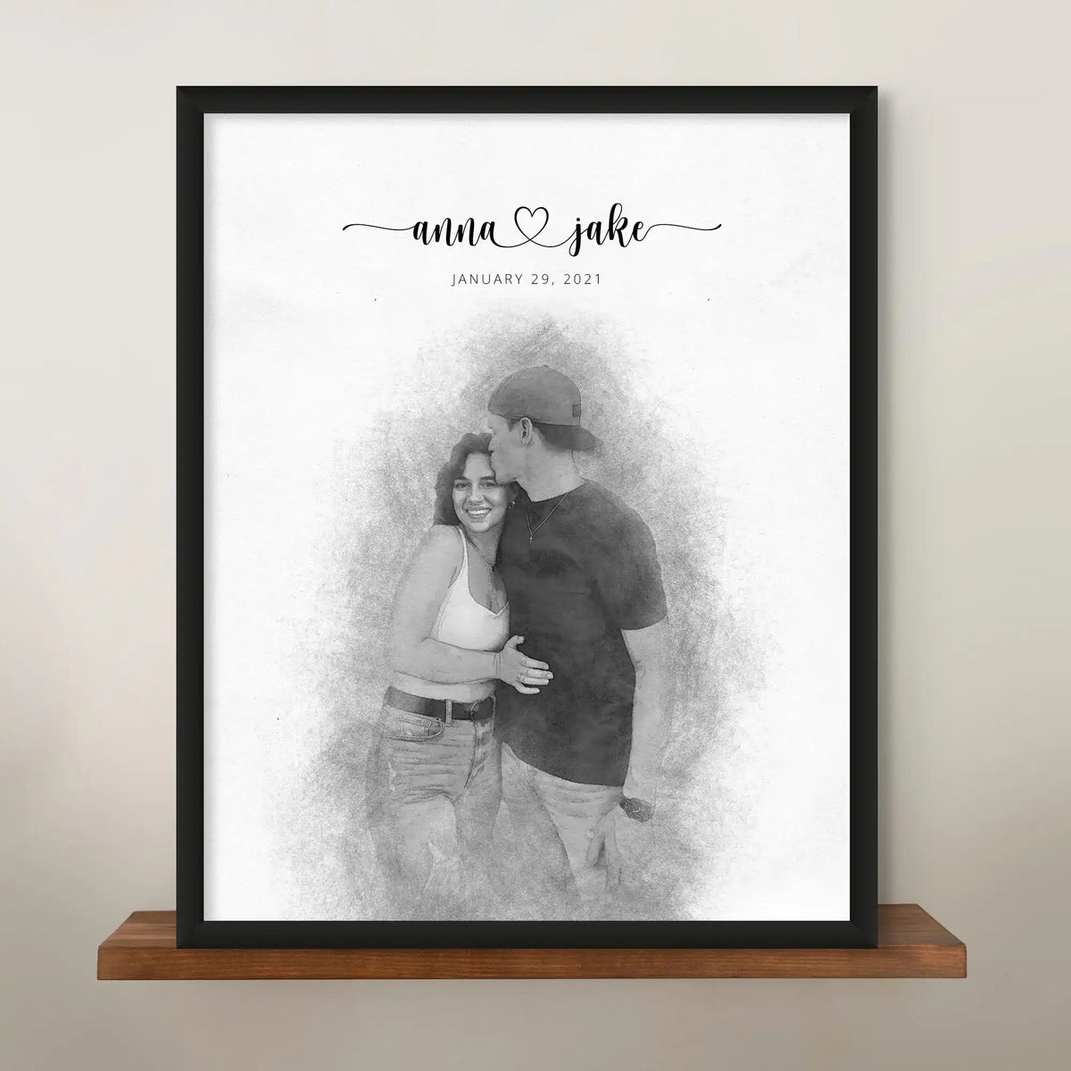 Sketch-style portrait of a couple, the man kissing the woman's forehead, in a black frame on a wooden shelf